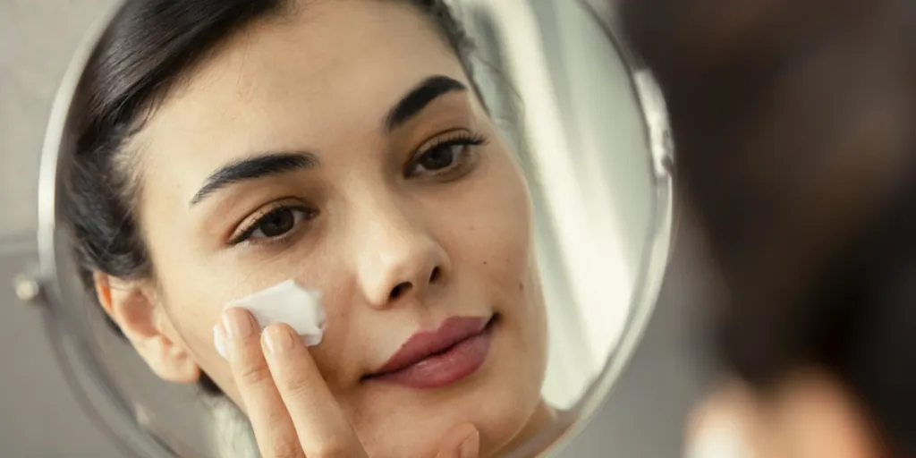 Woman with blemishes applying moisturizer to her face