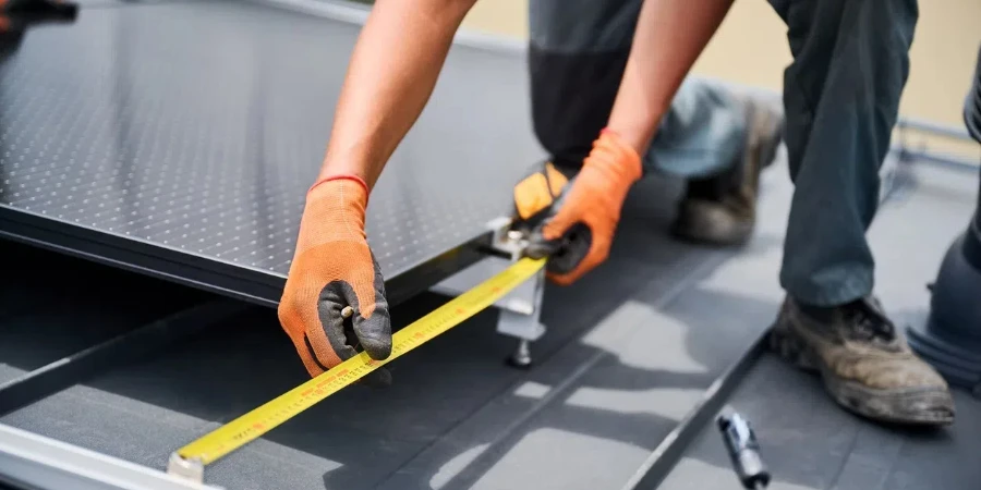 Worker building photovoltaic solar panel system, using ruler to measure mounting equipment.