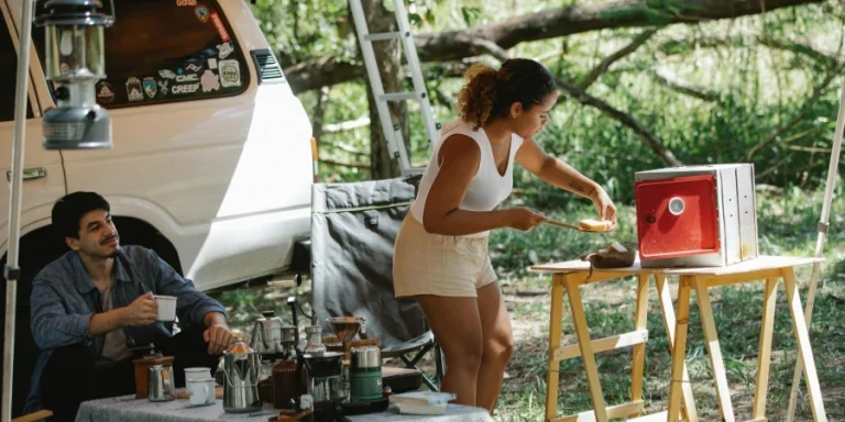 Joven étnica preparando sándwiches en una estufa portátil durante un picnic con su novio