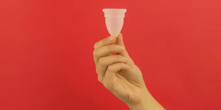 a hand holding a small plastic cup in front of a red background