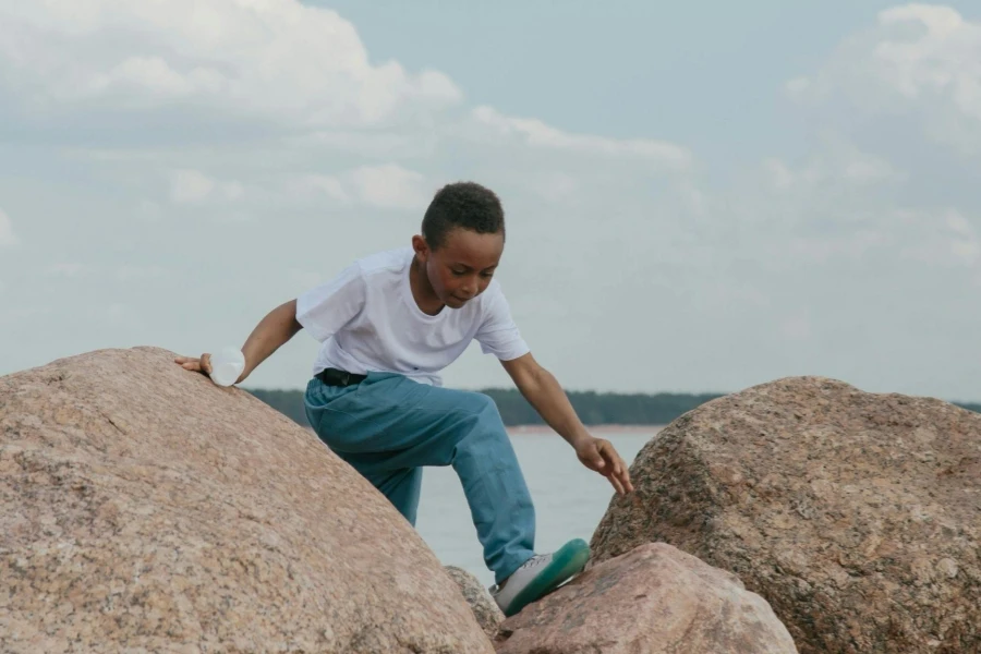 A Young Boy in White T-shirt and Blue Denim Jeans Climbing on Rocks