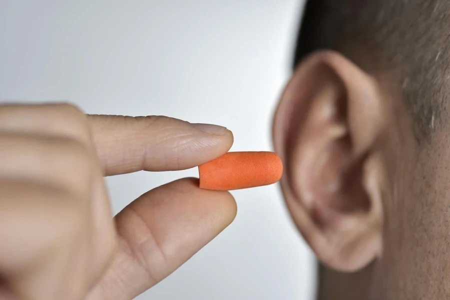 A man inserting an orange earplug in his ear