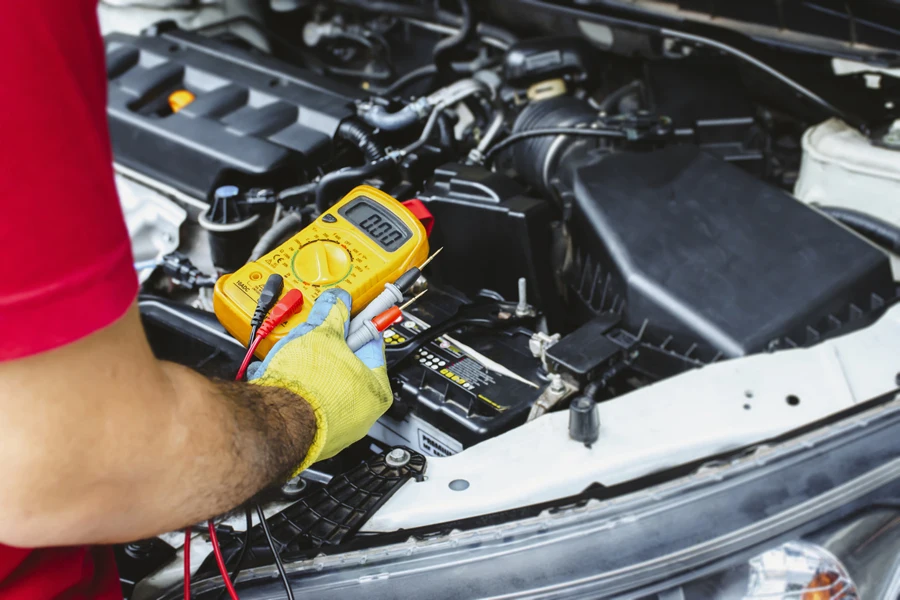 A mechanic holds a digital multimeter to check the car electrical system