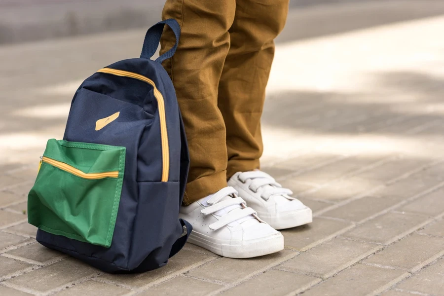 A schoolboy standing with a backpack in brown pants