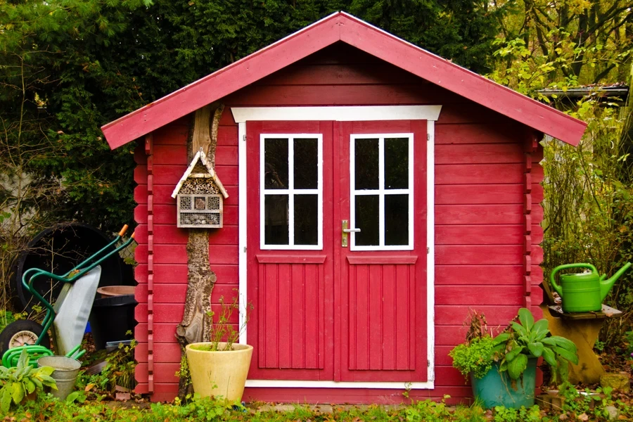 A small red potting shed in a garden setting