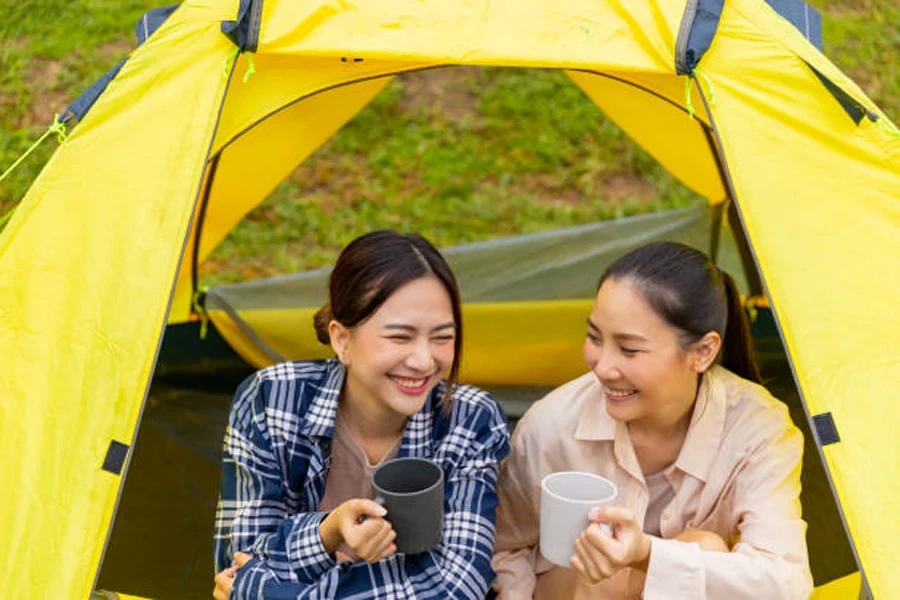 Asian Woman Friends Drinking Coffee Together in the Tent While Camping in Forest