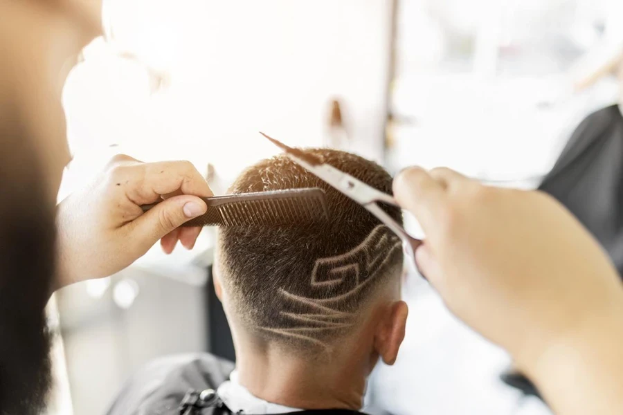 Barber shaves a design into a client's hair holding scissors