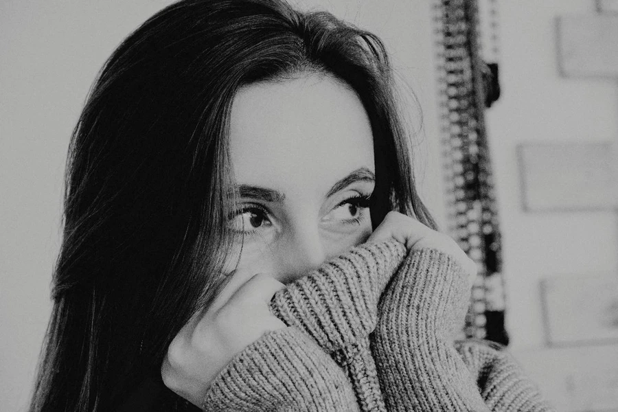 Black and white of female in warm sweater covering face with collar and looking away