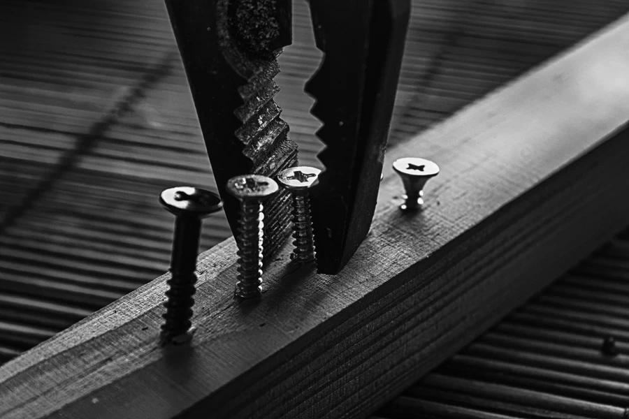 Close-up of pliers removing screws from wood