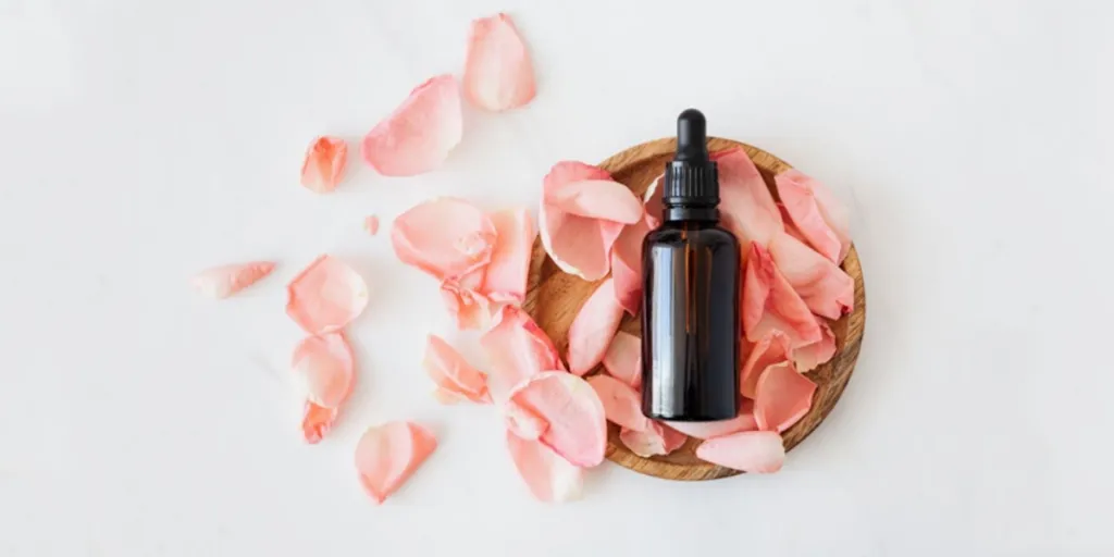 Cosmetic bottle in a wooden plate next to pink rose petals