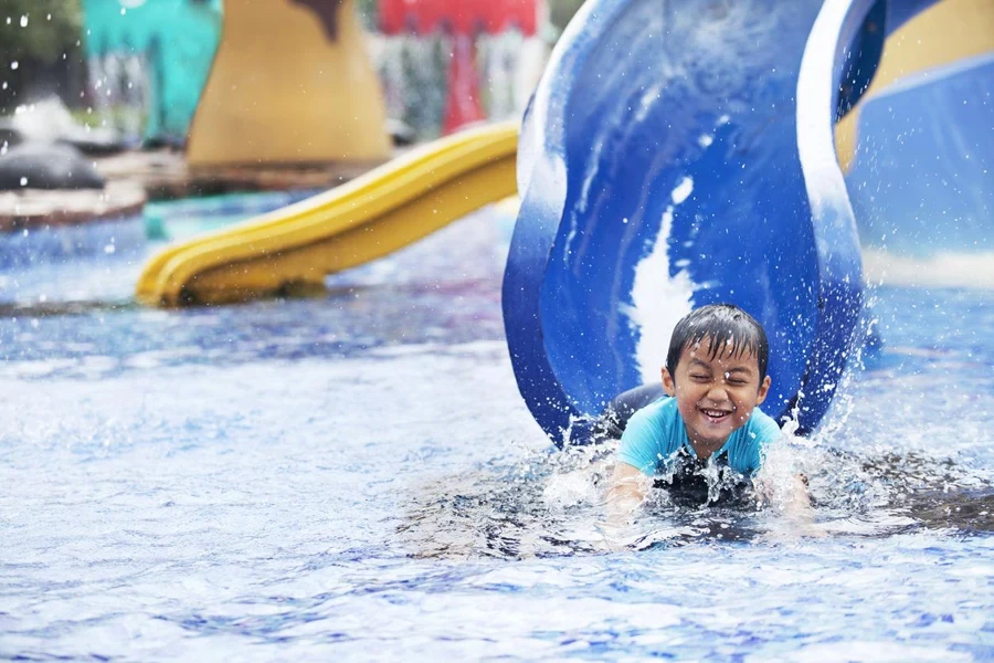 Cute asian boy having fun splashing into pool after going down water slide