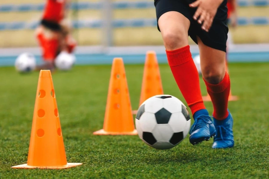 Footballer dribbling ball on training between orange cones