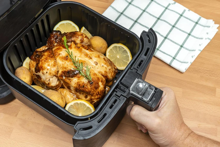 Hand Cooking Whole Roast Chicken with Garnish in Air Fryer in Kitchen