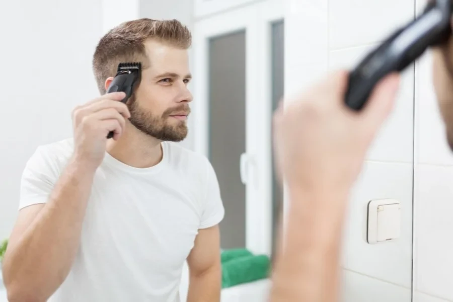 Handsome man cutting his own hair with a clipper