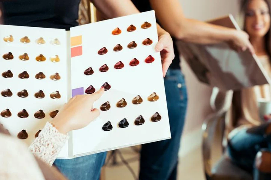 Happy young woman and hairdresser choosing hair color, samples from palette in salon