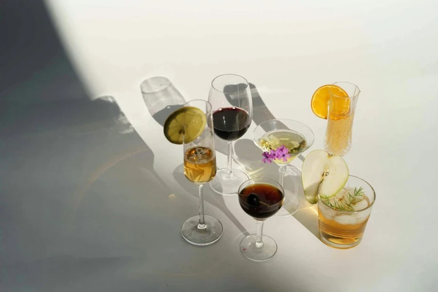 High angle of assorted alcohol drinks including red wine with champagne Manhattan and Martini cocktail near glass of pear brandy