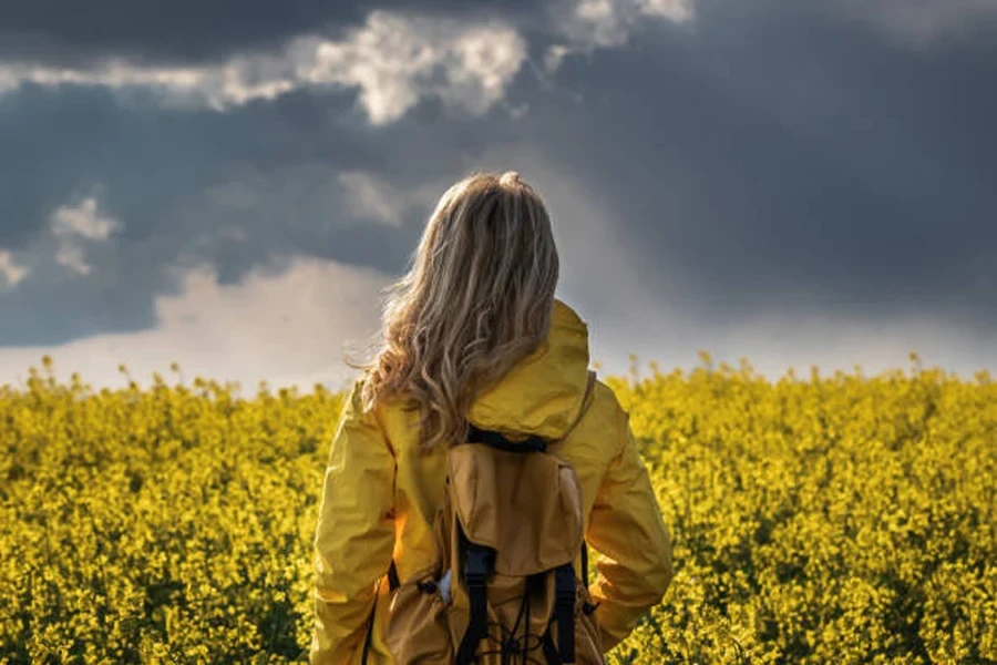 Hiking Woman Standing in Rapeseed Field and Looking at Cloudy Sky