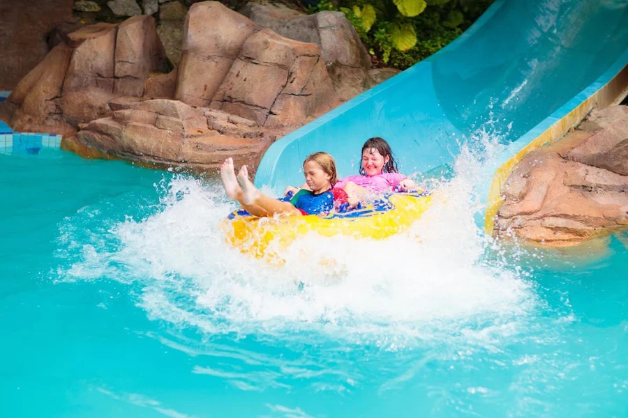 Kids on water slide in outdoor swimming pool.