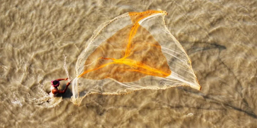 Man throwing large knotless net into muddy water