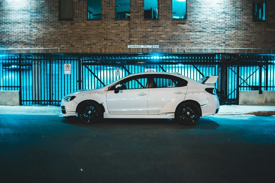 Modern automobile with black wheels and shiny white body on asphalt road near brick building behind fence