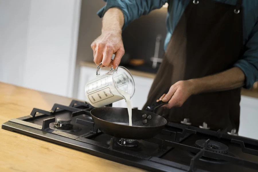 Person using a measuring jug to pour liquid into pan