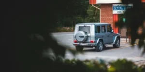 Сквозь зелень деревьев виден задний бампер современного вездехода, припаркованного на тротуаре возле городского здания