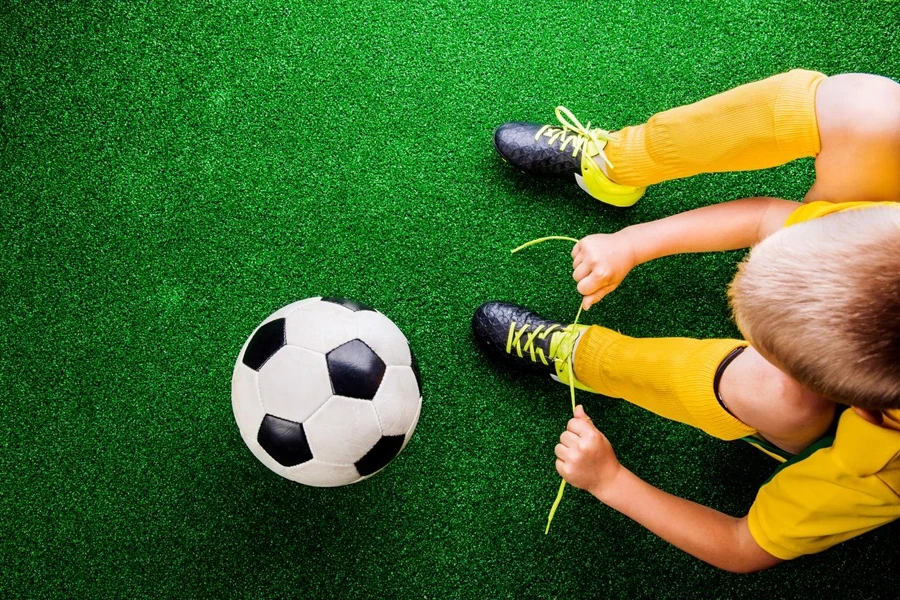 Unrecognizable little football player against green grass