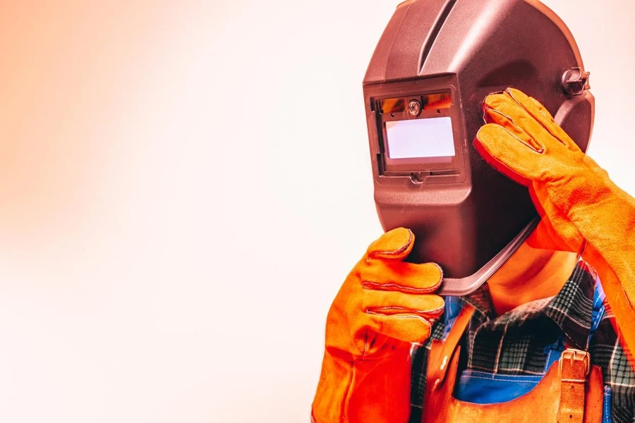 Welder in a protective suit, gloves, taking off his welding mask