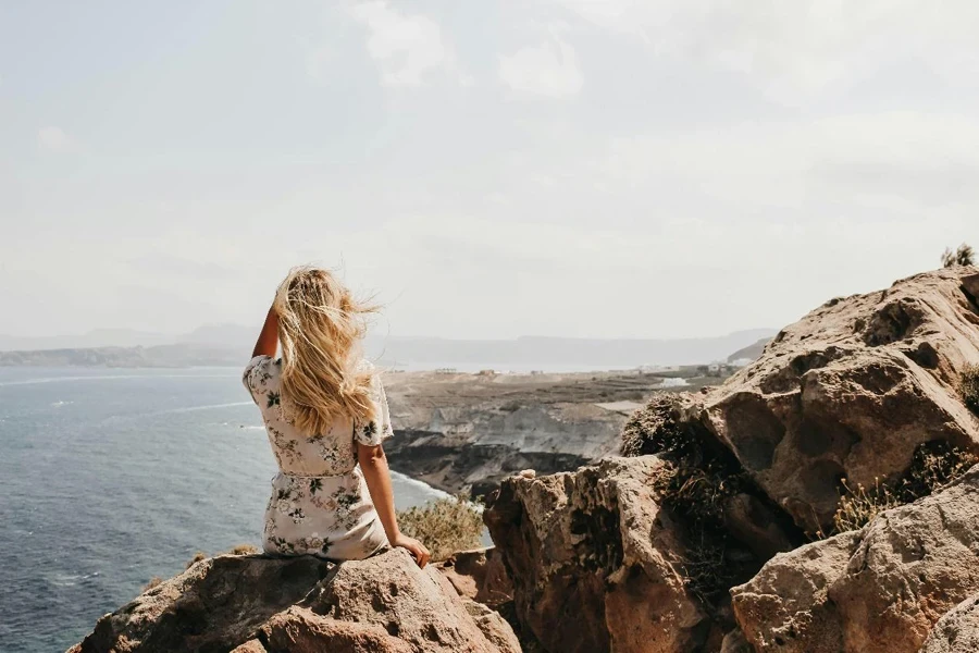 Woman Sitting on a Cliff Watching the Body of Water