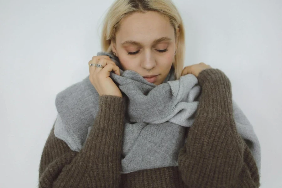 Woman in Gray Sweater Covering Her Face With Gray Scarf