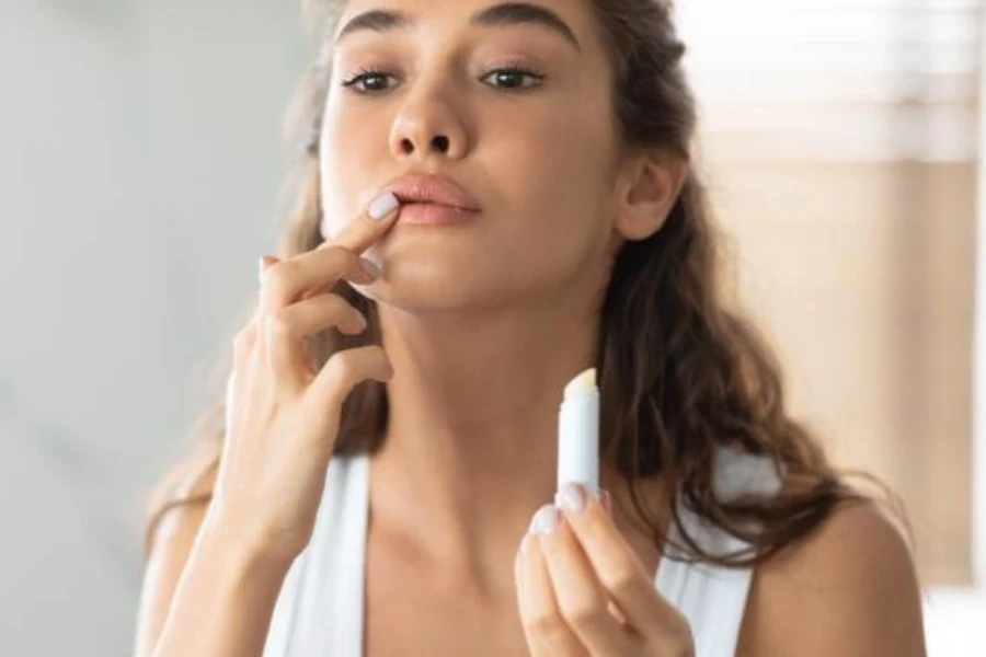 Young Lady Applying Lip Balm Moisturizing Skin In Bathroom Indoors