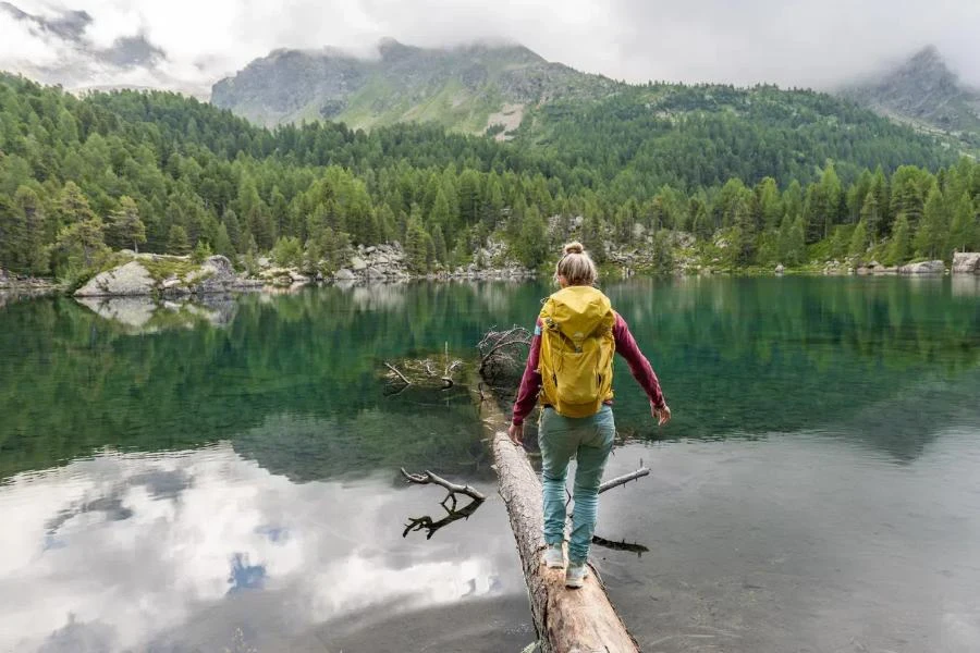 Young woman walks on tree trunk with a backpack