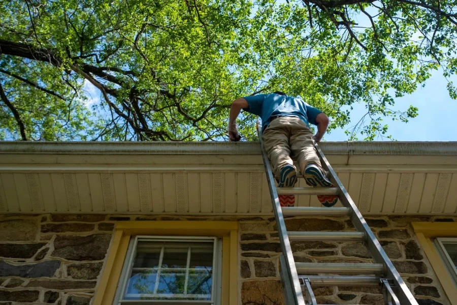 A man climbing a ladder to clean the gutter