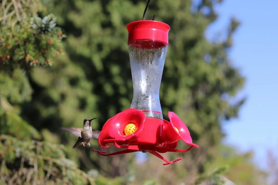 a red plastic hanging hummingbird feeder in a garden