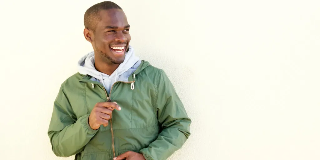 A smiling man in a green windbreaker jacket by the wall