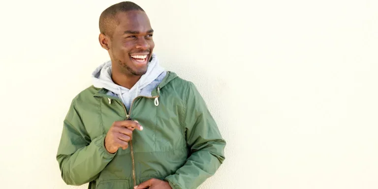 A smiling man in a green windbreaker jacket by the wall