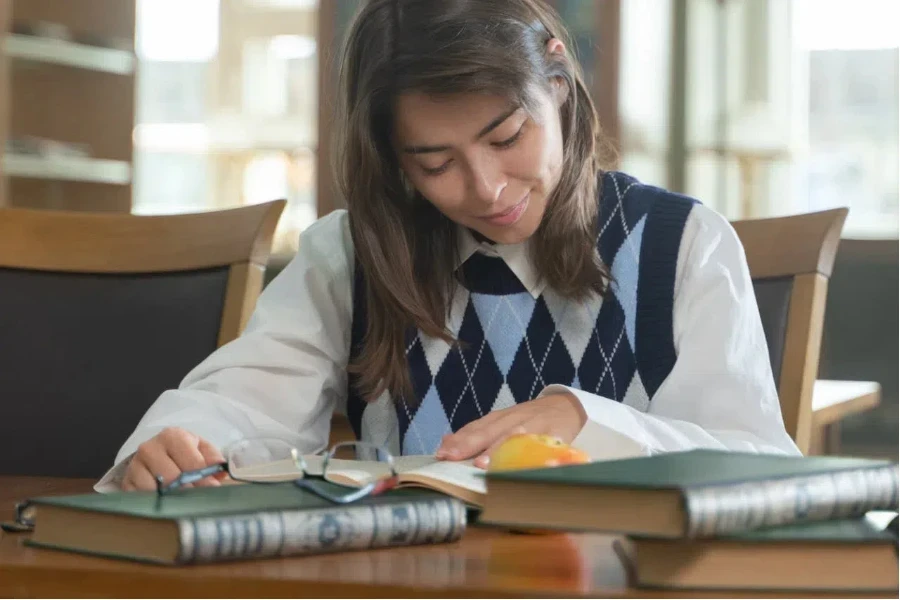 A woman wearing an argyle vest reading a book