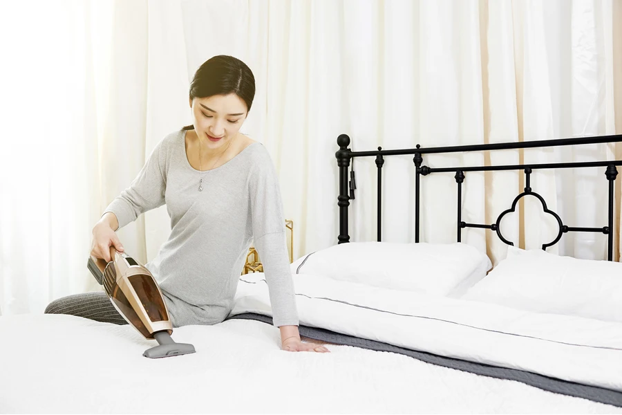 asian girl using a handheld vacuum to clean the bed