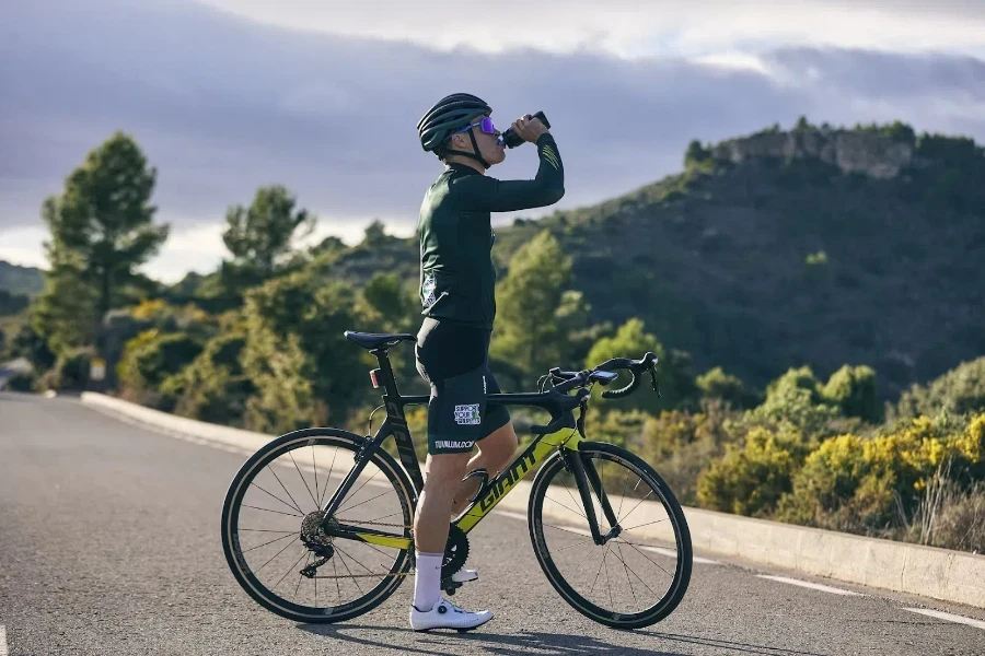 Cyclist standing on road while drinking from light water bottle