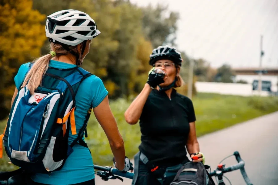 Female cyclists standing close with outdoor gear and hydration pack