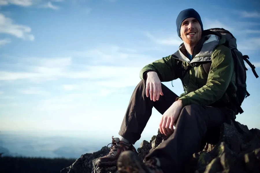 Man at a mountain top in a green outer shell windbreaker