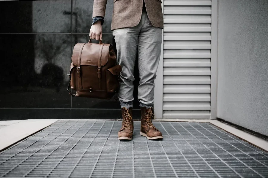 Man holding brown leather backpack next to wall