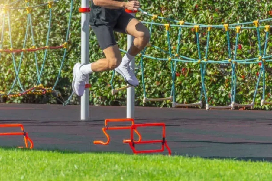 Man jumping over red collapsible agility hurdles at park