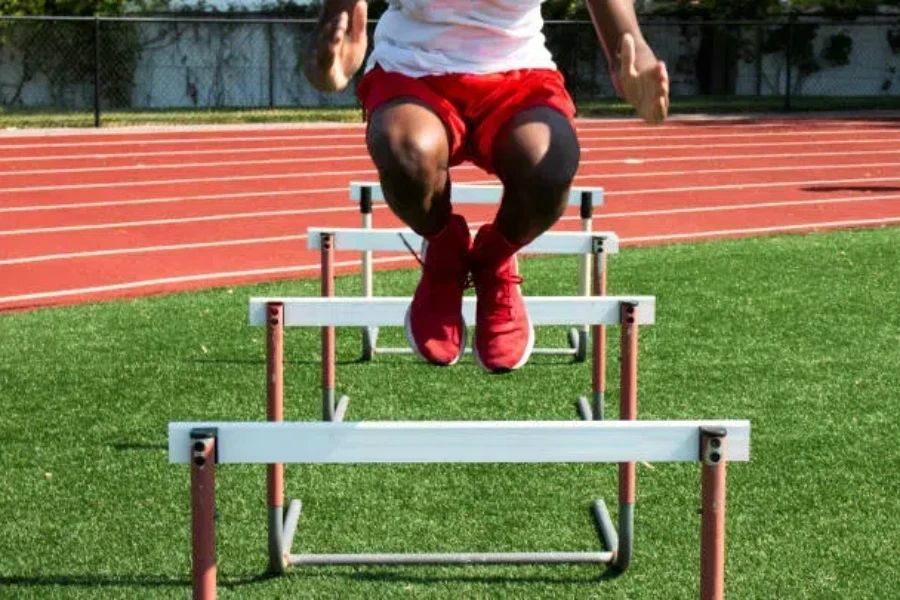 Man jumping over tall agility hurdles on grass