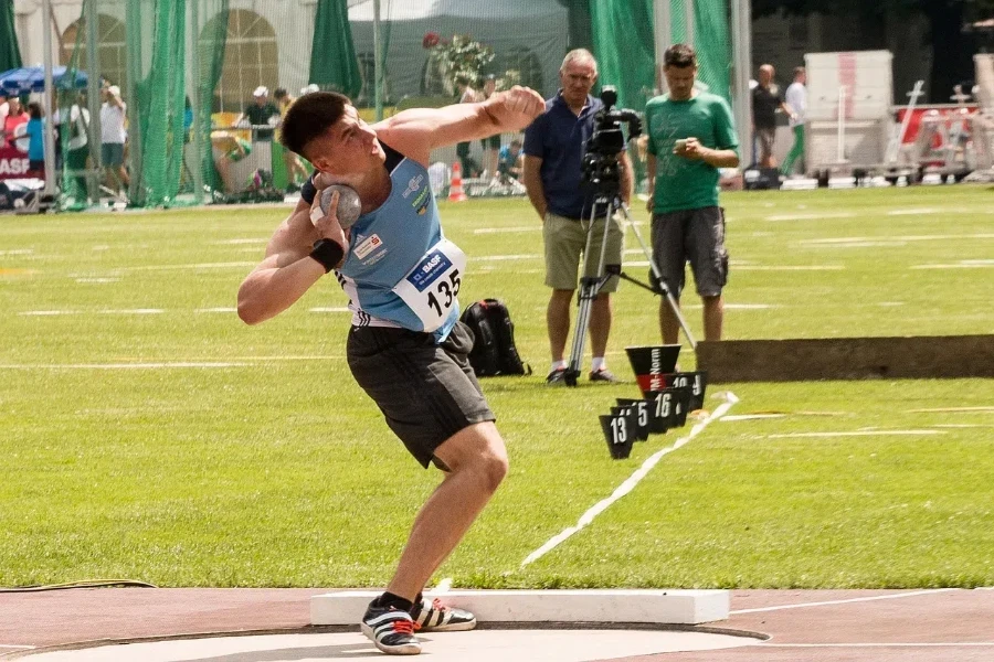 Man throwing a shot put ball near a toe board