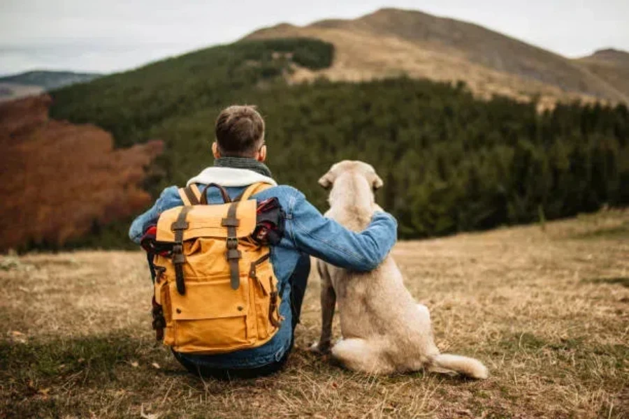 Man wearing yellow convertible backpack sitting with dog