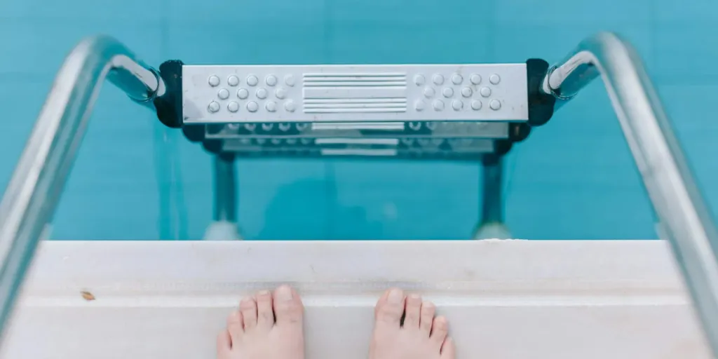 Two feet at the top of a metal pool ladder