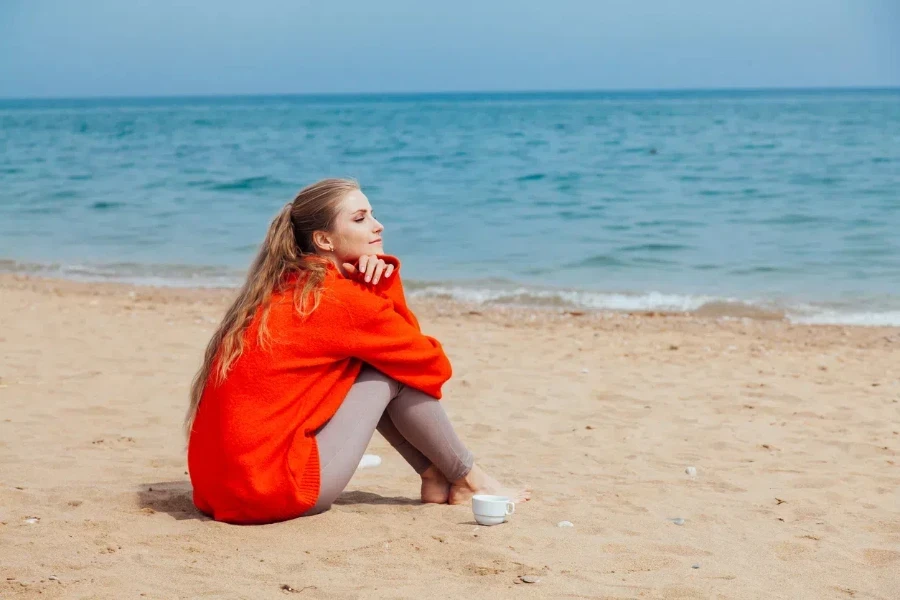 Woman by the beach wearing an oversized sweatshirt and leggings