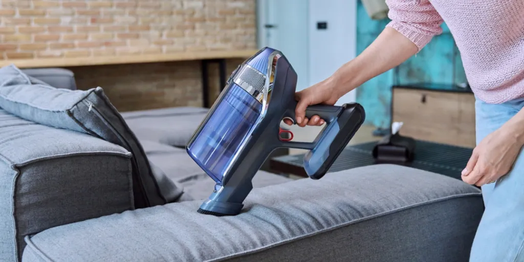 woman cleaning sofa with handheld vacuum cleaner