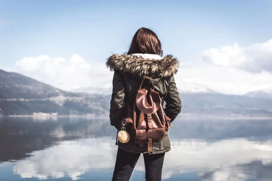 Woman looking at lake wearing brown leather backpack